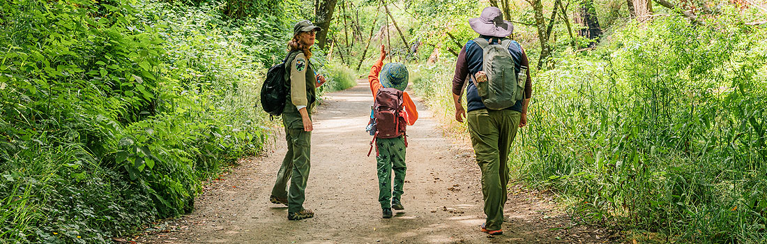 Parks naturalist walking on trail with a parent and child, talking together