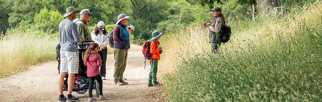 Parks naturalist in uniform speaking to a group of visitors along a trail