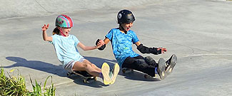 Two female students holding hands skateboarding at Valley Skate Park
